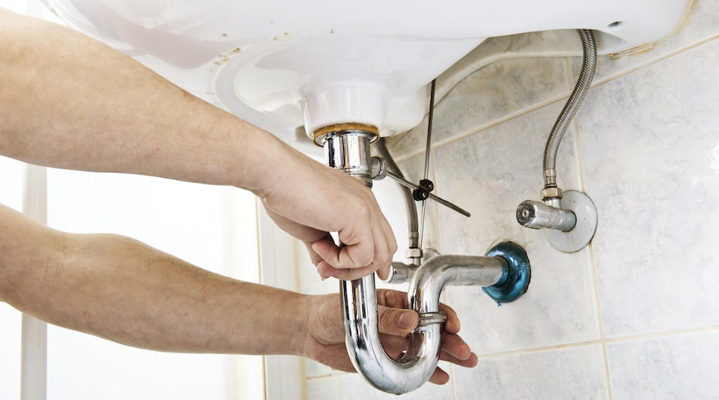 Bathroom Sink Replacement. Plumber using a wrench to loosen a siphon under a sink