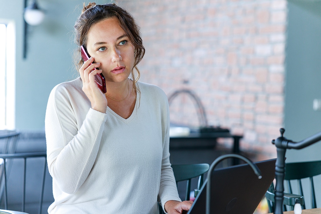 A woman holding a phone calling a plumber for faucet cartridge replacement.