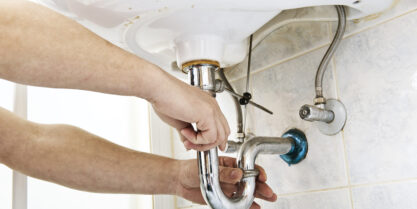 Bathroom Sink Replacement. Plumber using a wrench to loosen a siphon under a sink