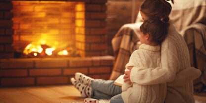 Two young sisters hugging front of cozy fireplace. Winter Plumbing Tips.
