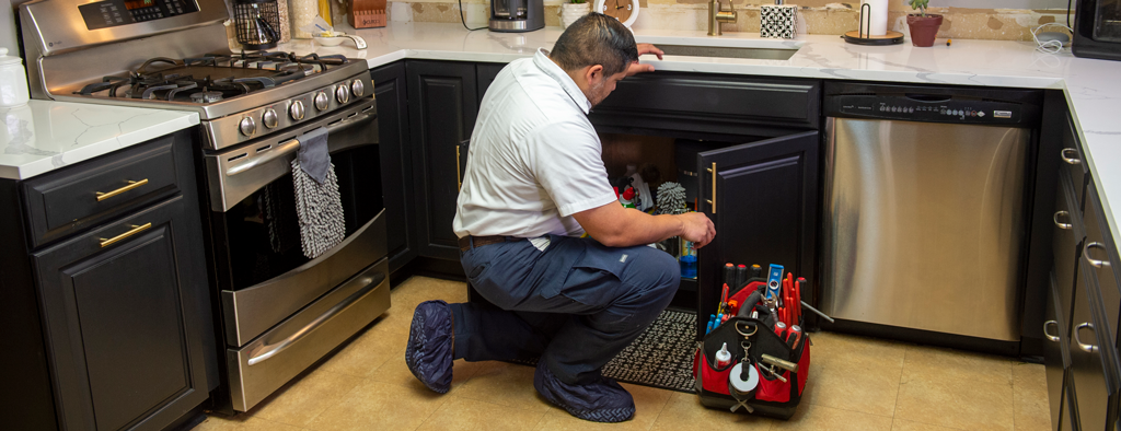 bluefrog technician looking under customer's kitchen sink | Types of tankless water heaters | bluefrog plumbing + drain