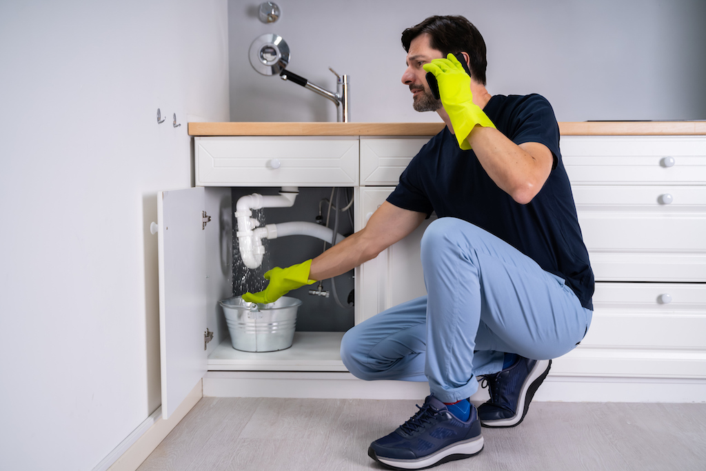 A pipe bursts under the sink and man calls emergency plumber. | Plumbing Service