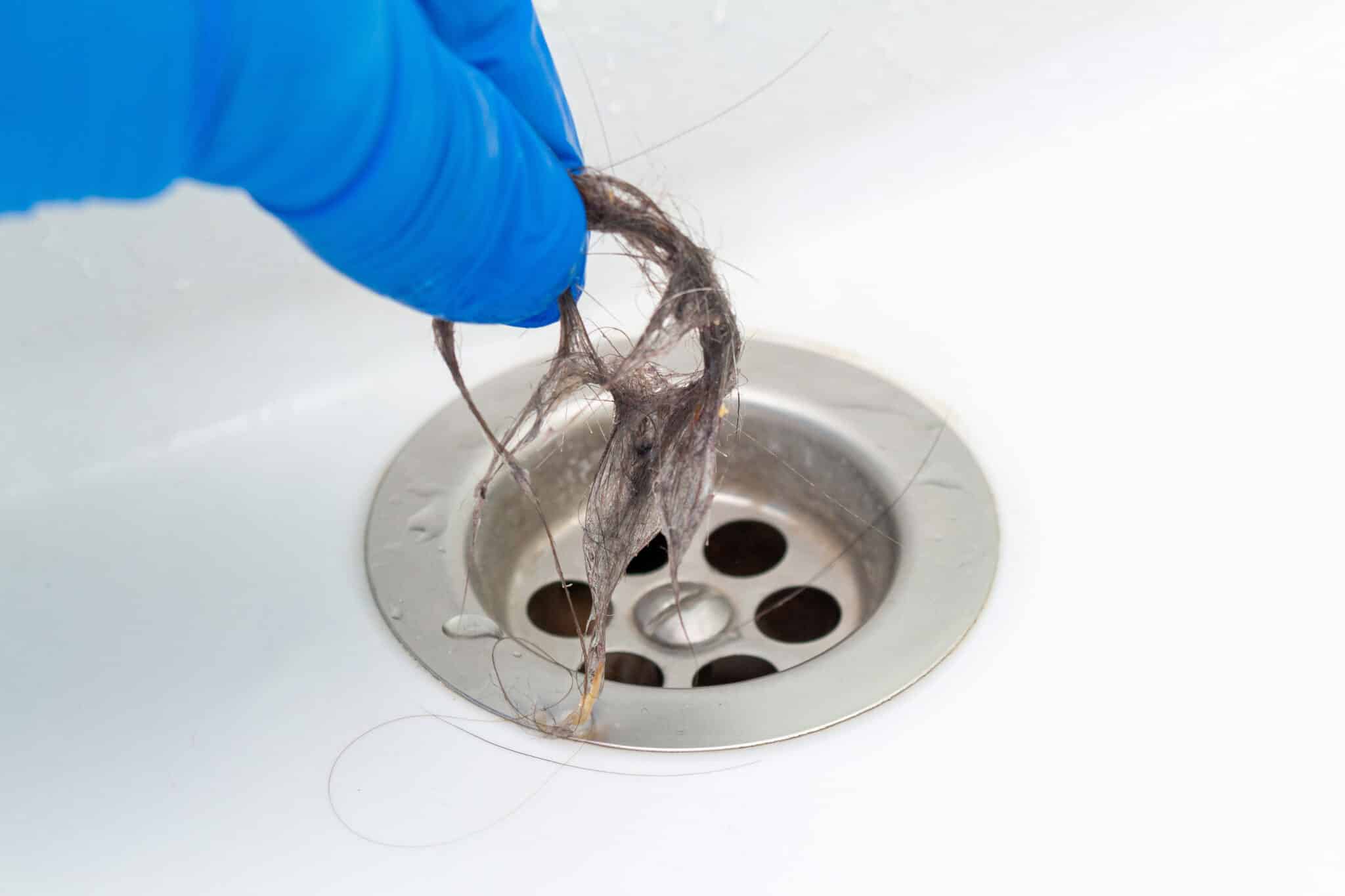 Hand in glove cleaning a clogged sink or bathtub drain from hair, Drain Cleaning.