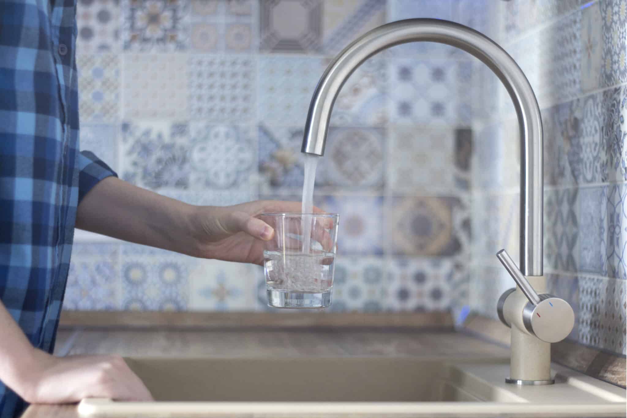 A woman in a blue plaid shirt pours water from the kitchen faucet into a glass for Pure Water Solutions