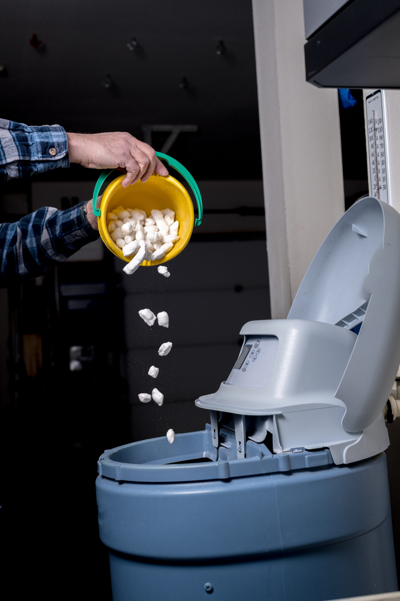 Man pours fresh salt pellets from a yellow bucket into high efficiency water softeners.