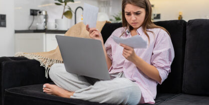 A woman sitting on a couch reviewing her water bill, which has increased due to hidden leaks.