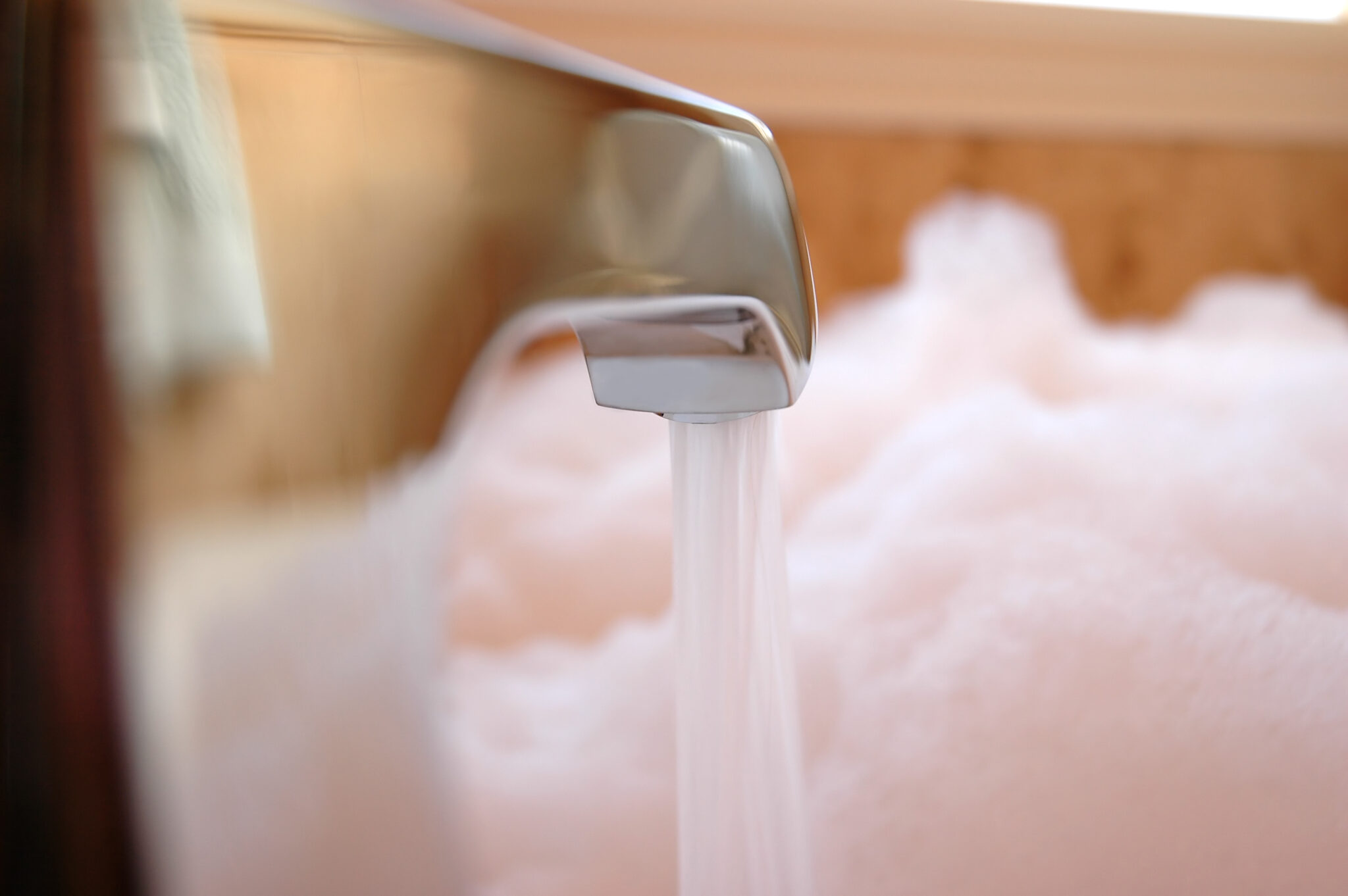 Close-up of a tub spout diverter faucet pouring water into a bubble bath.