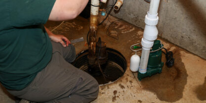A plumber repairing a sewage ejector pump in a flooded residential basement.